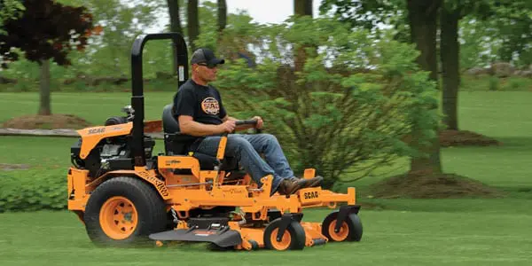 Man operating orange riding lawn mower.